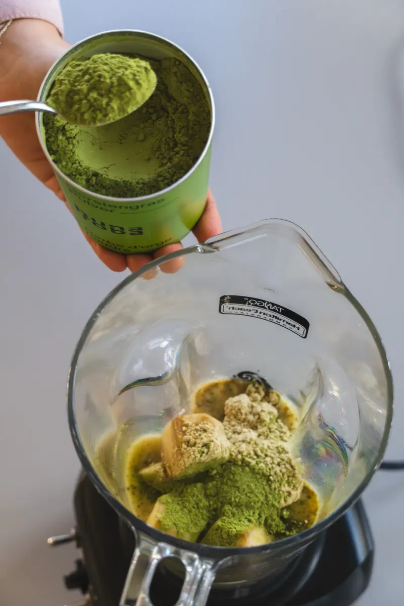 A spoonful of barley grass powder above a smoothie blender